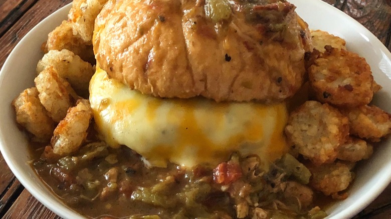 Burger in a bowl covered with green chile sauce and hash browns
