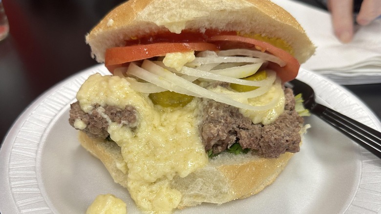 Steamed cheeseburger with cheese, onions, and tomatos on paper plate