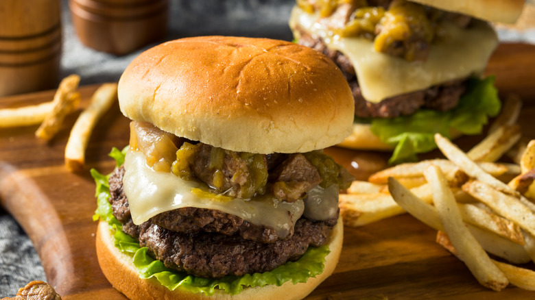 Two green chile cheeseburgers with double patties on wooden board with fries
