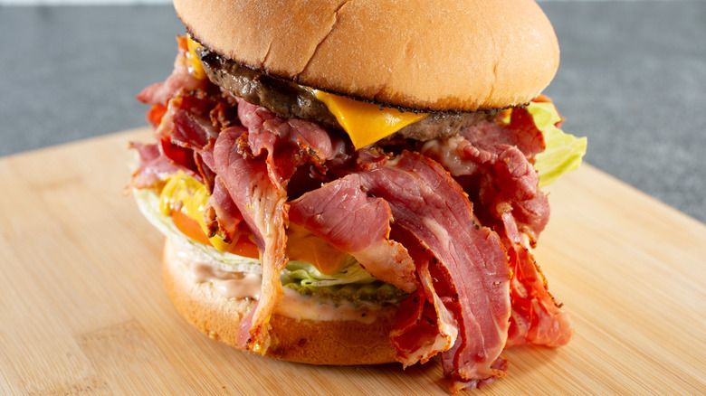 Hamburger with slices of pastrami on wooden board