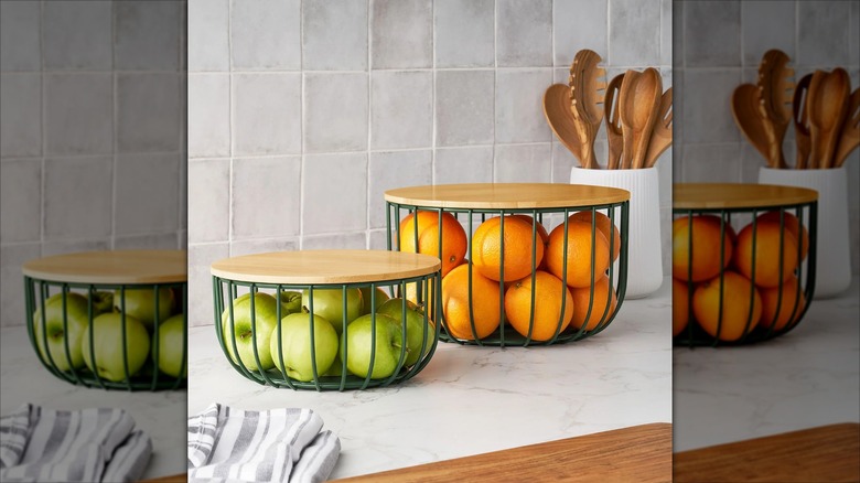 Wire bowls with lids holding apples and oranges on a kitchen counterop