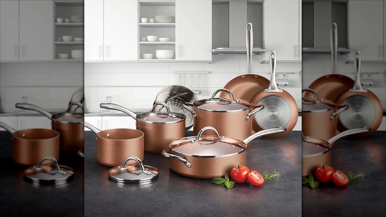 Copper cookware set on kitchen counter with tomatoes and herbs