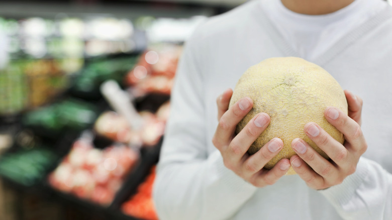 Person examining cantaloupe at grocery store