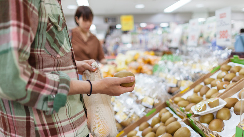 Person examining a kiwi at grocery store