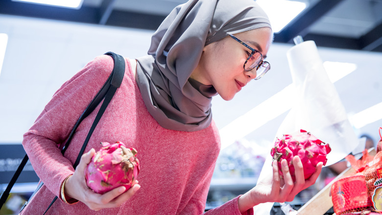 Woman examining dragon fruit at grocery store