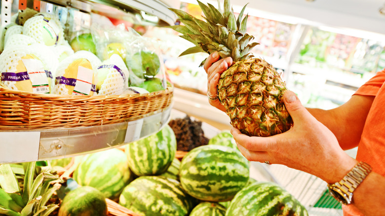 Person examining pineapple in grocery store