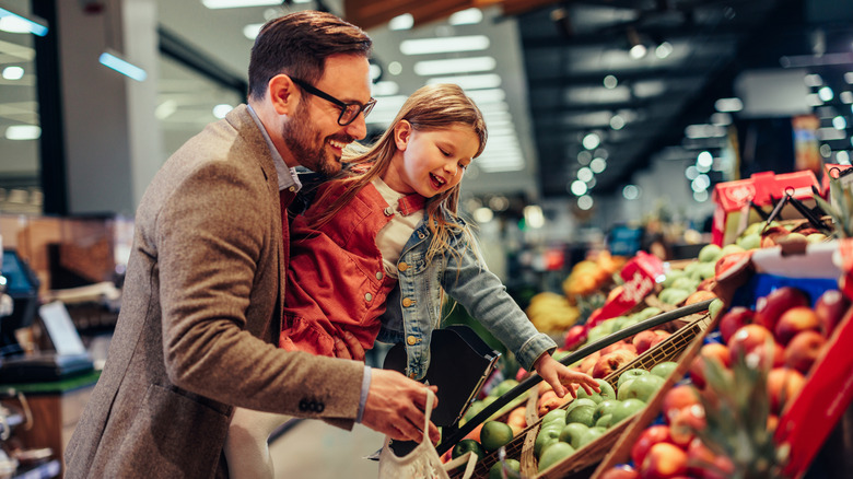 Father and daughter picking out apples at grocery store