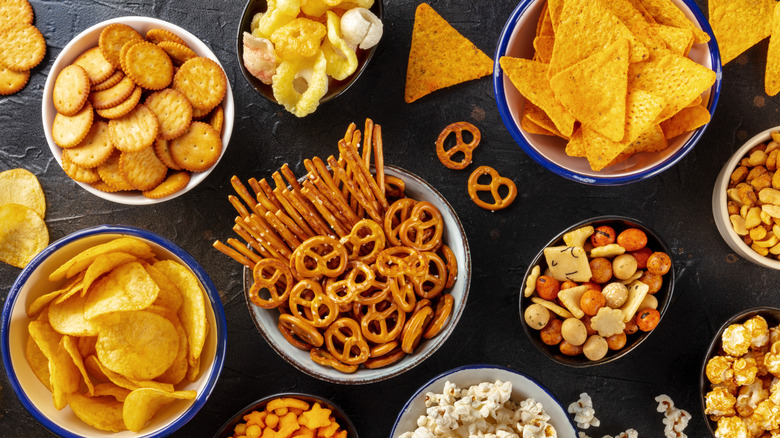 An assortment of salty snacks in bowls on a dark table