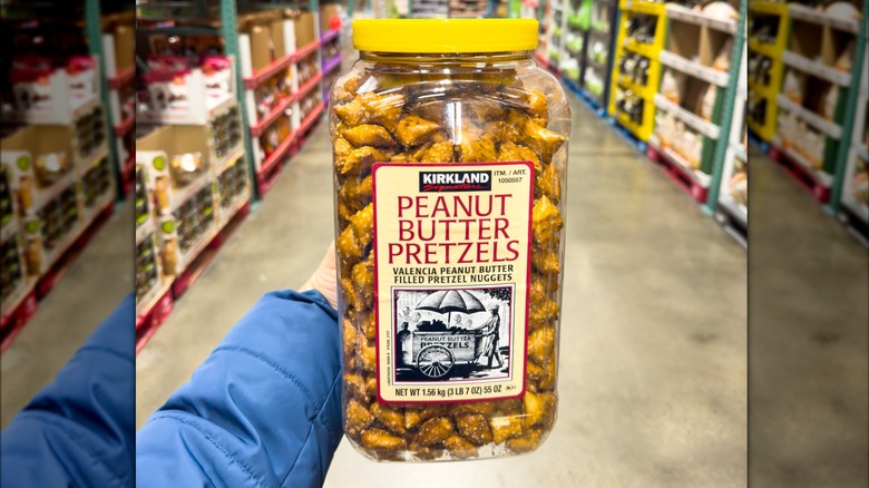 Large transparent container with a yellow lid filled with peanut butter pretzels, pictured in a Costco aisle