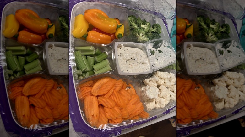 An open veggie platter with several raw vegetables and ranch dip on the middle