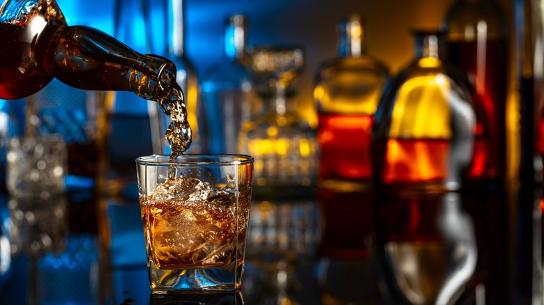 Alcohol being poured into a glass with a range of blurred bottles in the background