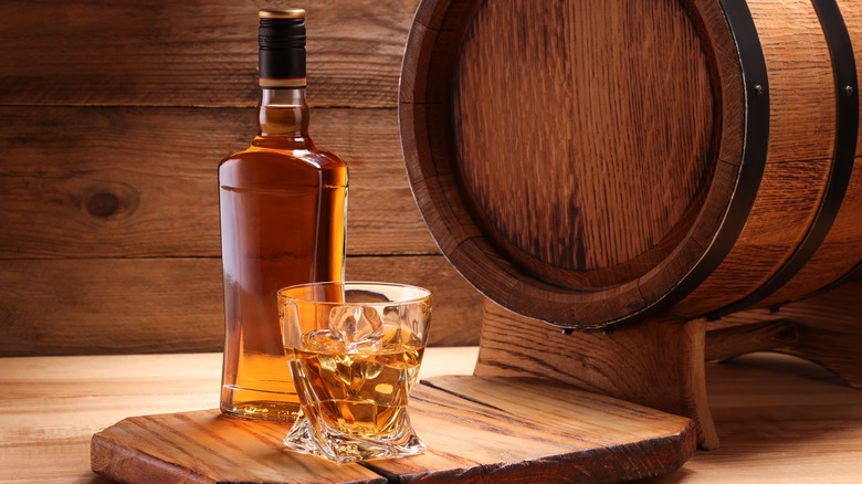 An unbranded bottle of whiskey next to a full whiskey glass and a barrel