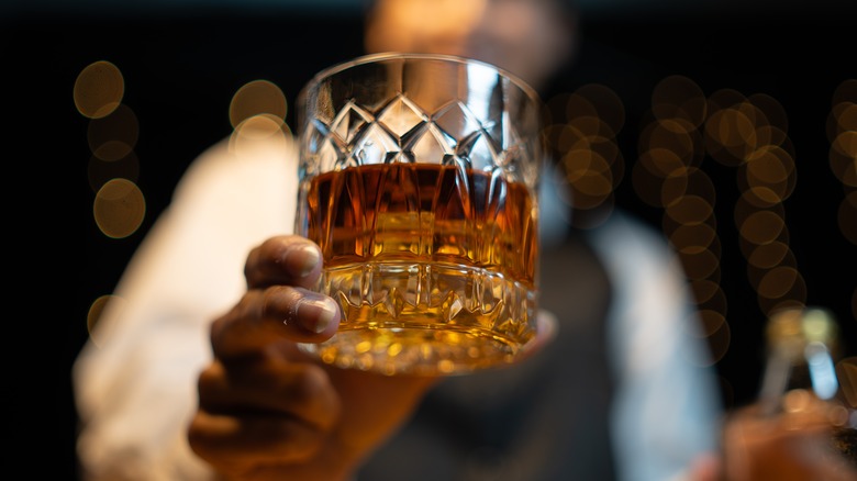 A close up of a bartender holding up a glass of whiskey to the camera