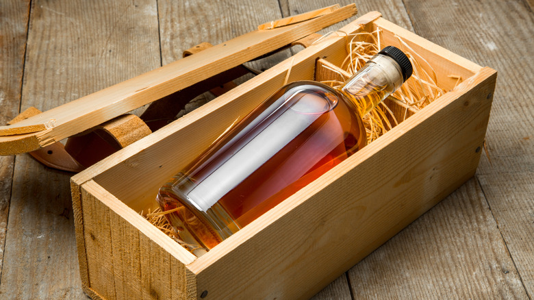 An unbranded bottle of dark spirits in a wooden gift box protected by straw