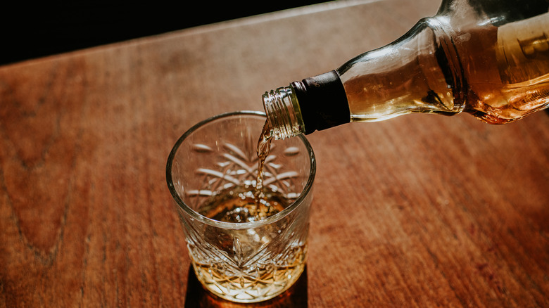 Whiskey being poured into a glass which is sat on a table