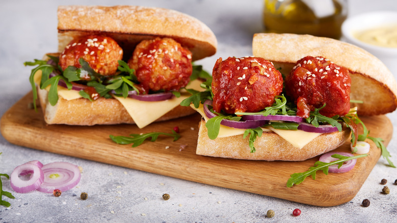 Meatball subs with fresh greens, red bell peppers, unmelted cheese slices, and sesame seeds on a toasted bun