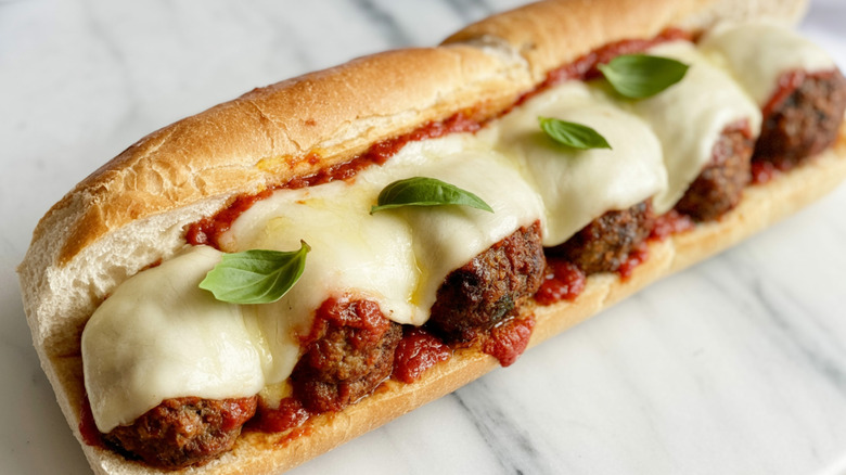 Meatball sub topped with melted cheese and basil leaves on a marble countertop