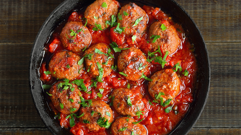 Meatballs in thick tomato sauce in iron skillet topped with shredded herbs on a wooden table