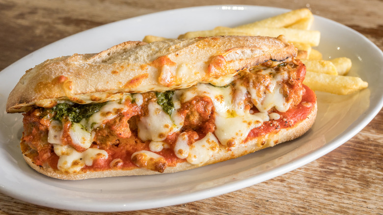 Toasted meatball sub with lots of melted cheese on a plate with French fries