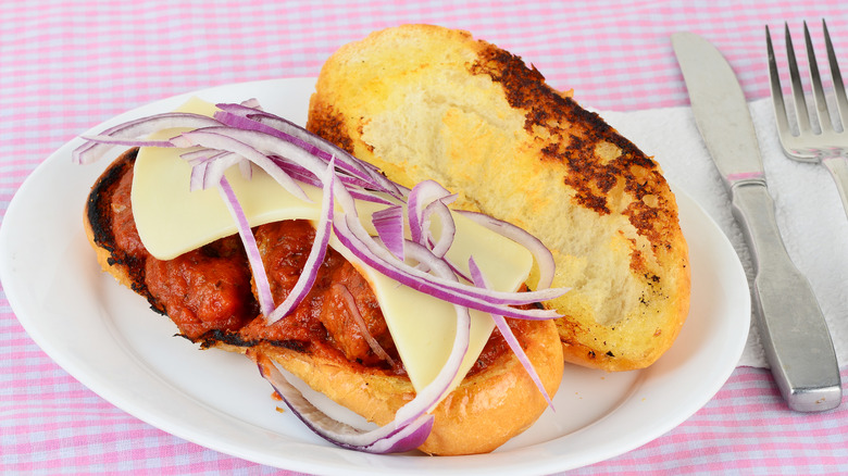 Meatball sub made with buttery garlic bread and topped with red onions on a pink and white checkered tablecloth