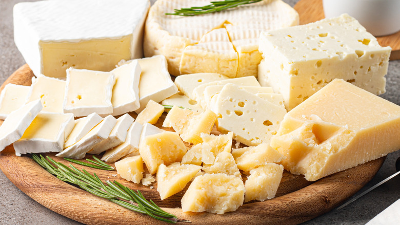 A wooden platter featuring several types of cheese and fresh rosemary
