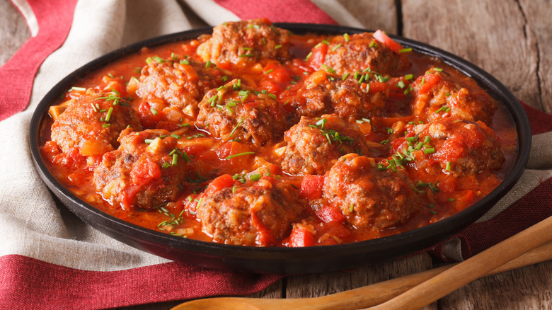 Meatballs in a platter of thick tomato sauce with wooden spoons and napkin on wooden table