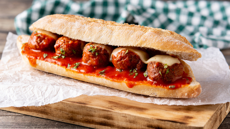 Meatball sub sitting on top of a paper wrapper on a cutting board near a green checked napkin