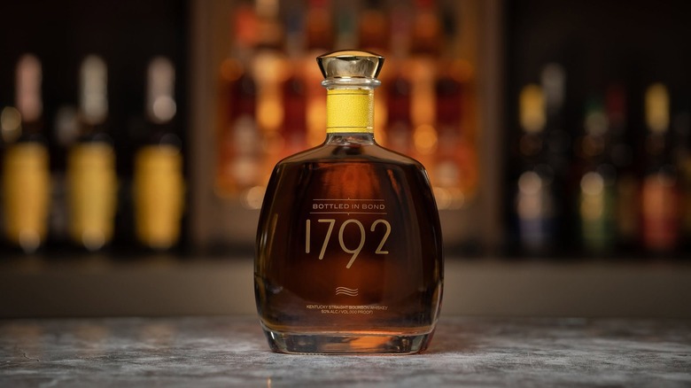 1792 Bottled-in-Bond posed on a lit surface with blurred bottles shown in the background
