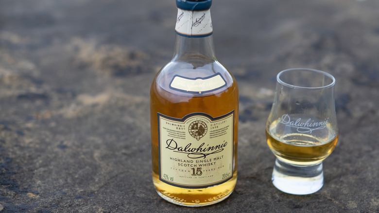 A bottle of Dalwhinnie 15-year placed on a rocky surface next to a filled glass
