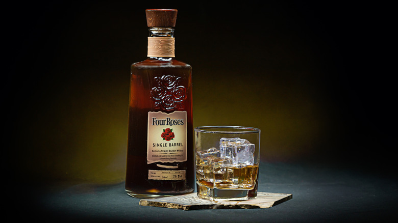 A stylized product shot of Four Roses Single Barrel next to a filled glass in front of a dark background