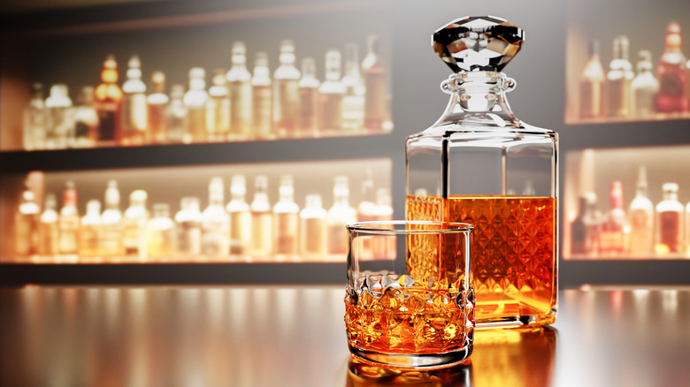 A glass of whisky in front of a decanter with shelves of blurred bottles in the background