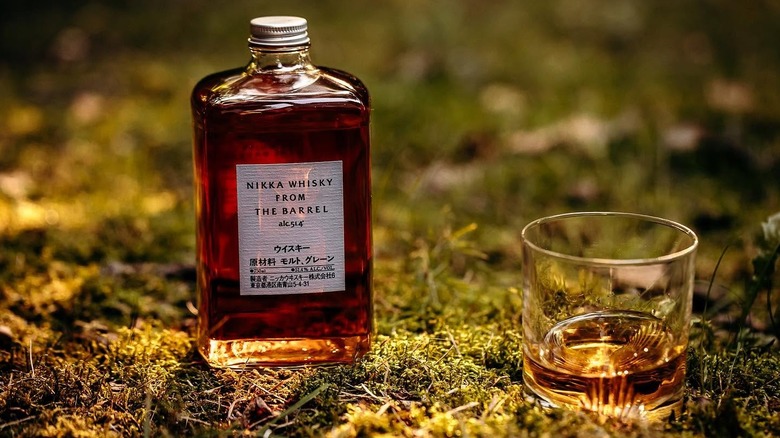 A bottle of Nikka From The Barrel on a mossy surface next to a filled glass