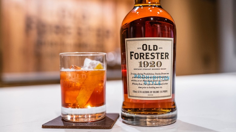 A bottle of Old Forester 1920 next to a cocktail in a branded glass
