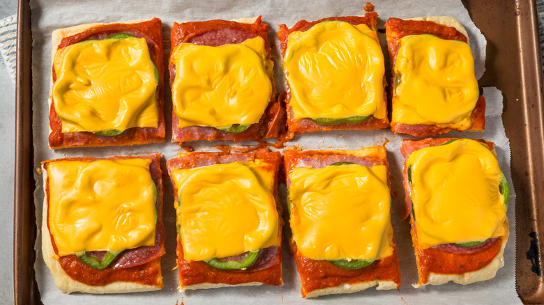 A tray of eight square pizza slices with green pepper and melted American cheese on top
