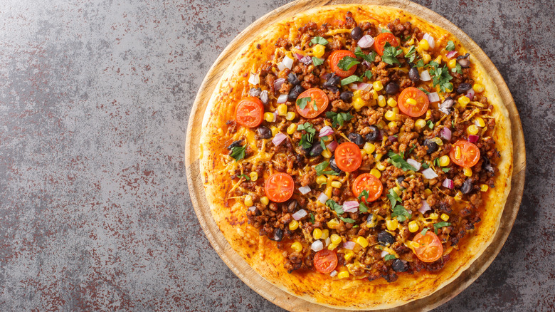 A pizza with corn, beans, onions, herbs, and cherry tomatoes on a slate grey background