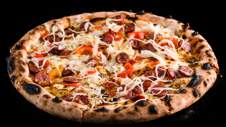 A neapolitan-style pizza with a charred crust and sauerkraut, meat, and peppers on a black background