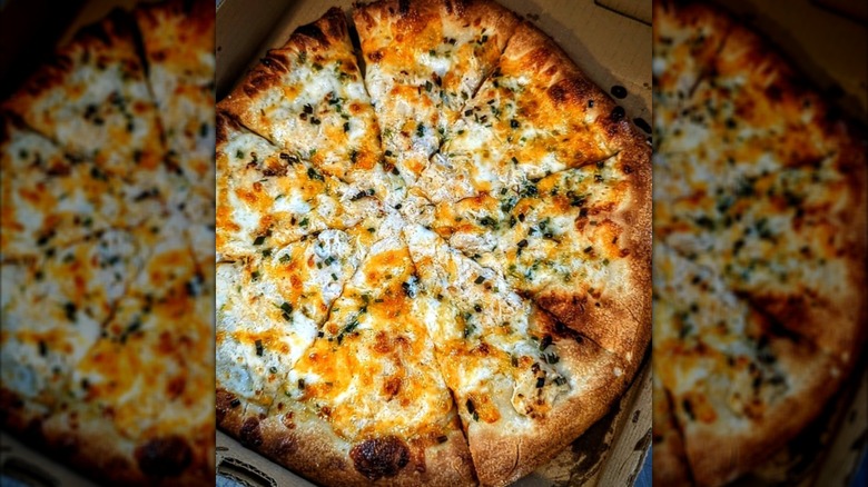 A creamy crab dip pizza with fresh herbs in a box