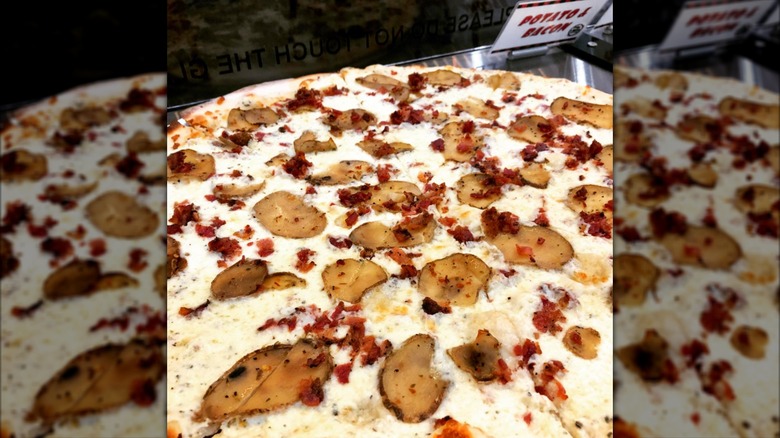 A close-up of a pie with thin-sliced potato, bacon, and alfredo sauce