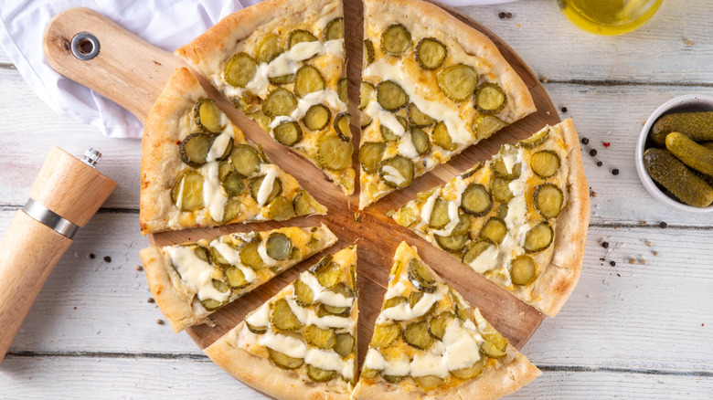 A small pickle pizza with a drizzle of creamy sauce on a round wood board