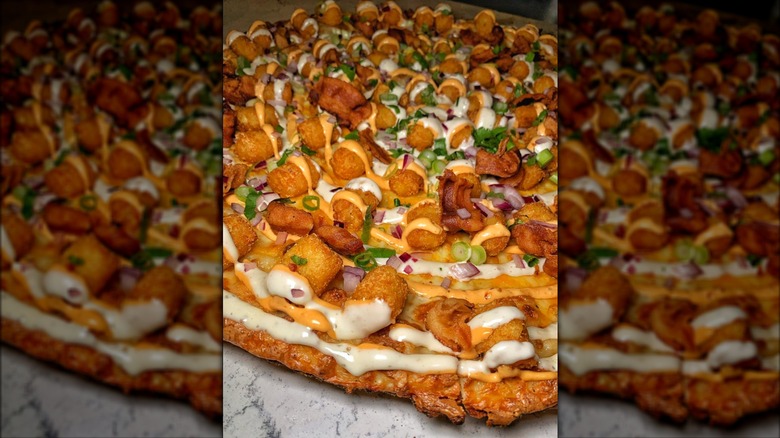 Close up of a thin-crust pizza pie with tater tots, sauces, and fresh herbs