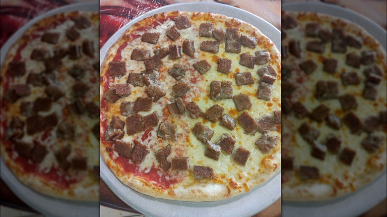 A thin crust pizza with square chunks of scrapple and cheese on a round metal backing pan