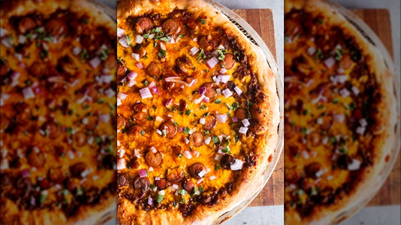 A homemade pizza with chili, fresh herbs, onions, and hot dog slices