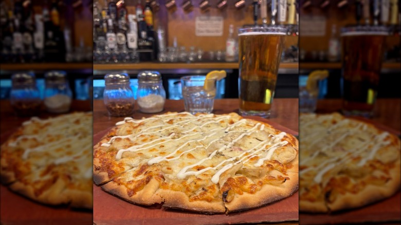 A pizza in a tavern with pierogi fillings, plenty of cheese, and a drizzle of white sauce