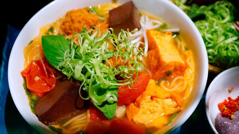 close up of white dish of Bún riêu cua (Tomato and crab noodle soup)