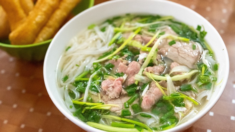 A steaming bowl of phở bò is served with fried dough sticks at a casual eatery in Hanoi