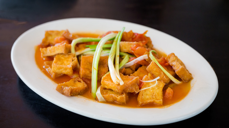 white plate of tofu with tomato sauce against dark background