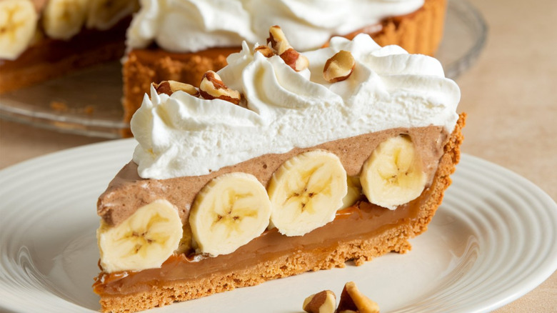 A slice of banoffee pie topped with chopped walnuts on a white plate