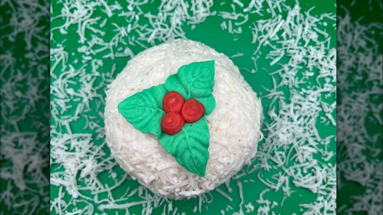 A top view of a scoop of ice cream rolled in coconut with an icy holly sprig on a green background