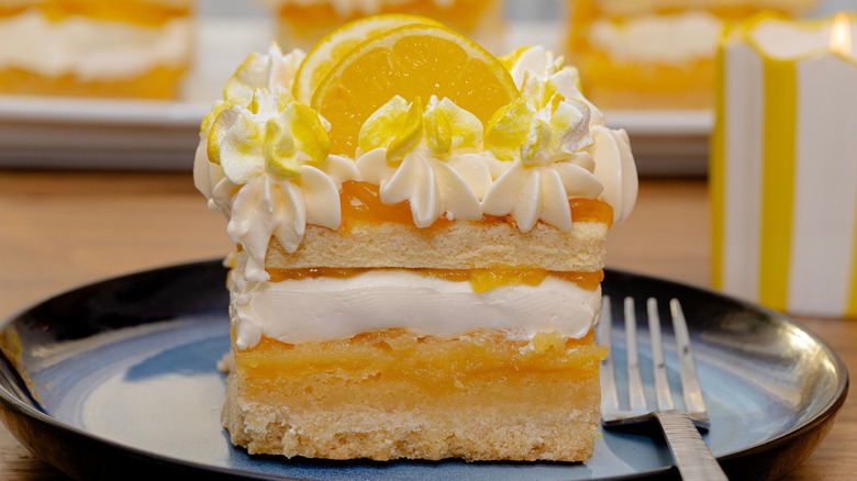 A layered lemon lush dessert on a blue plate with a fork