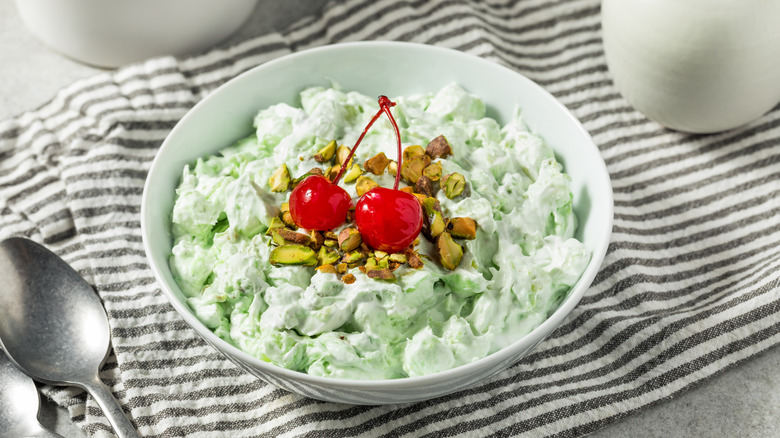 Watergate salad with a cherry on top in a white bowl on a striped cloth